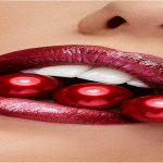 Open mouth with red liptisck biting red pearls in close up