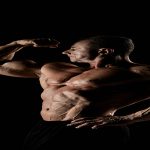 torso of attractive male body builder on black background.
