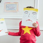 child holding two paintings with happy and sad faces